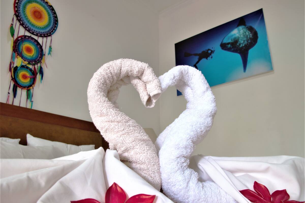 Cama com lençóis brancos e flores vermelhas, um sonho capturado e um quadro de baleia na parede.