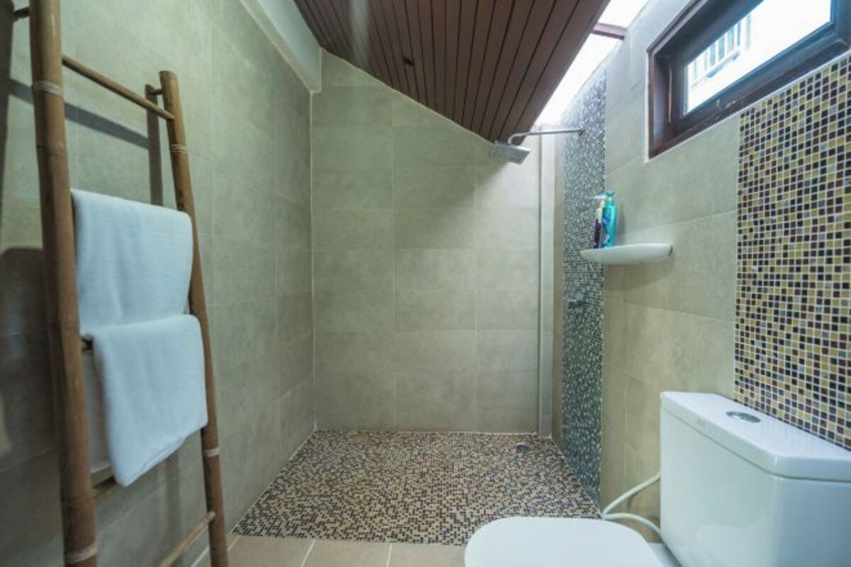 A small, enclosed shower area with a tiled floor, a toilet, and a shelf with toiletries.