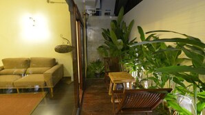 A cozy indoor space with a sofa, wooden chairs, and large green plants. - Yi's Garden Villa (Chiang Mai)