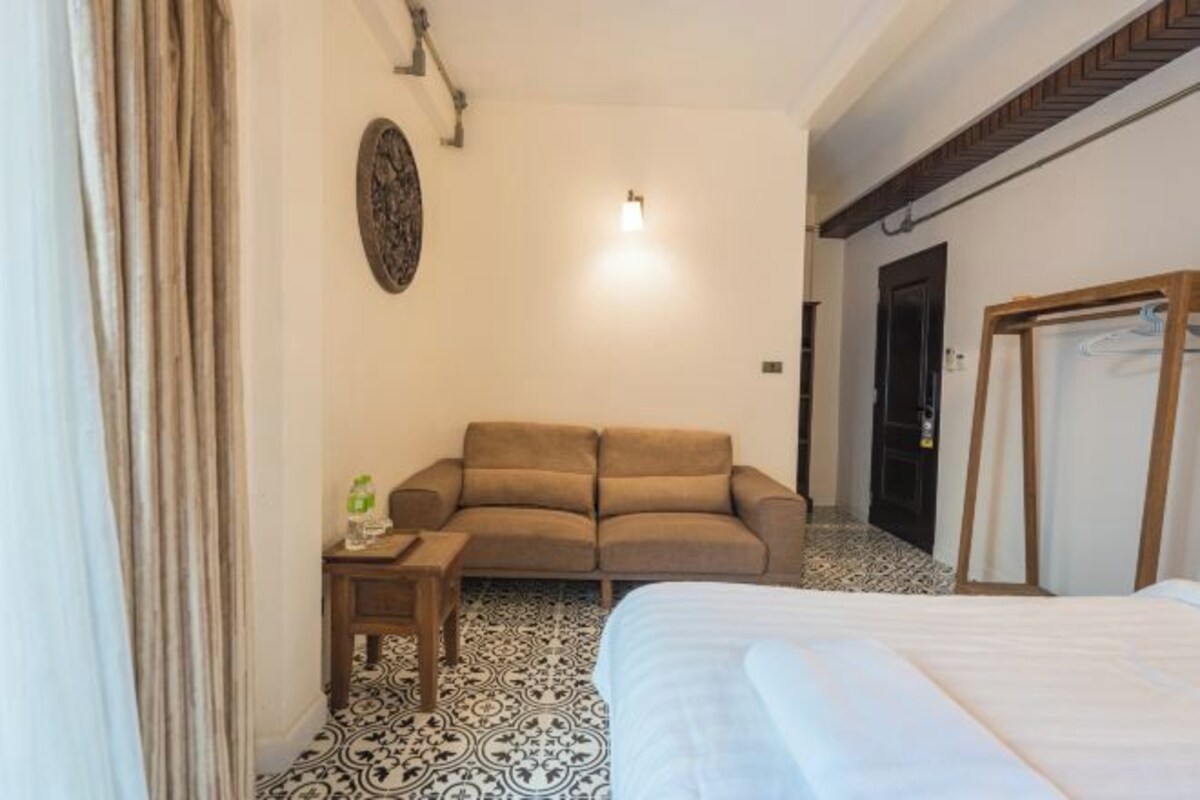 A hotel room with a bed, a sofa, a small table with a bottle, and a patterned floor.
