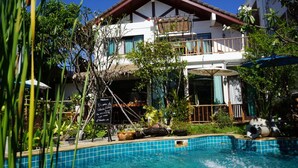 A two-story building with a pool, surrounded by lush greenery and a thatched roof structure. - Yi's Garden Villa (Chiang Mai)