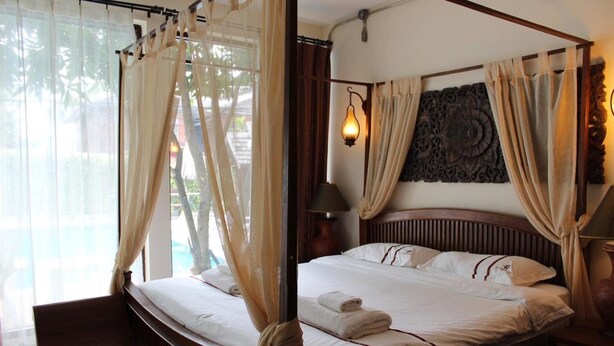 A four-poster bed with white linens and a canopy, a wall-mounted lamp, and a decorative headboard. - Yi's Garden Villa (Chiang Mai)