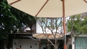 A poolside area with lounge chairs, a large umbrella, and a stone basin. - Yi's Garden Villa (Chiang Mai)
