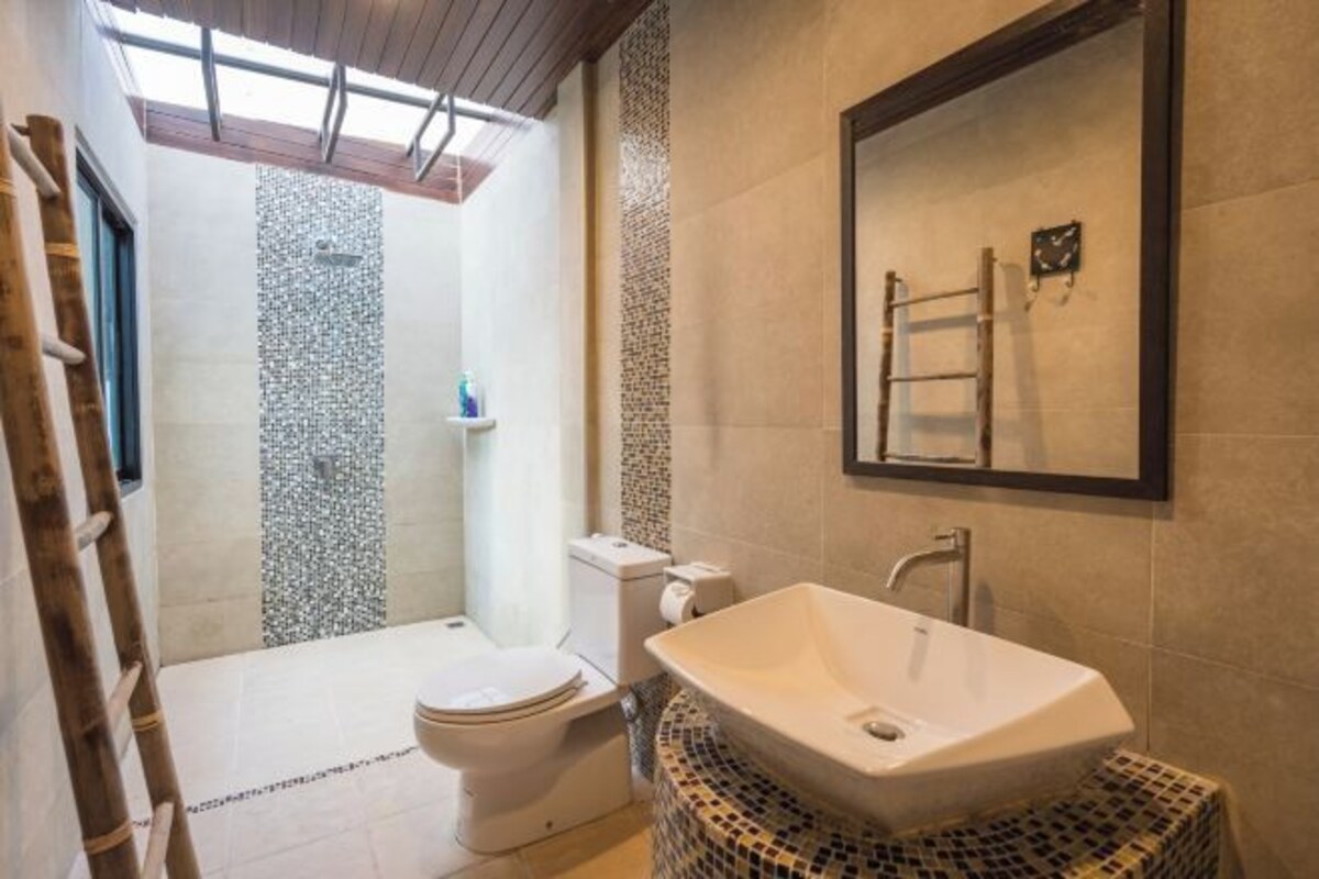 A bathroom with a large mirror, a freestanding sink, a toilet, and a shower.