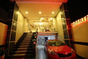 A hotel entrance with a staircase leading to the reception area, a red car parked outside, and a sign indicating 'APARTMENTS'.