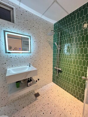 A bathroom with a white sink, a mirror, a shower with green tiles, and speckled flooring. - New Hotel & Apartment (Ho Chi Minh City)