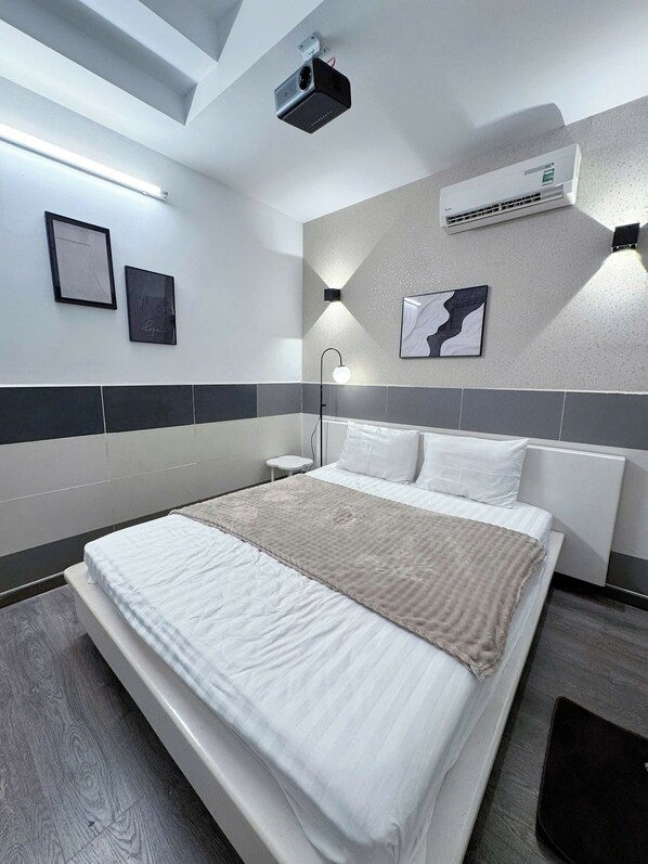 A modern hotel room with a bed, a projector, an air conditioner, and wall-mounted artwork. - New Hotel & Apartment (Ho Chi Minh City)