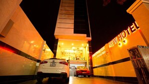 Entrada de un hotel nuevo por la noche, con dos coches aparcados frente a él.