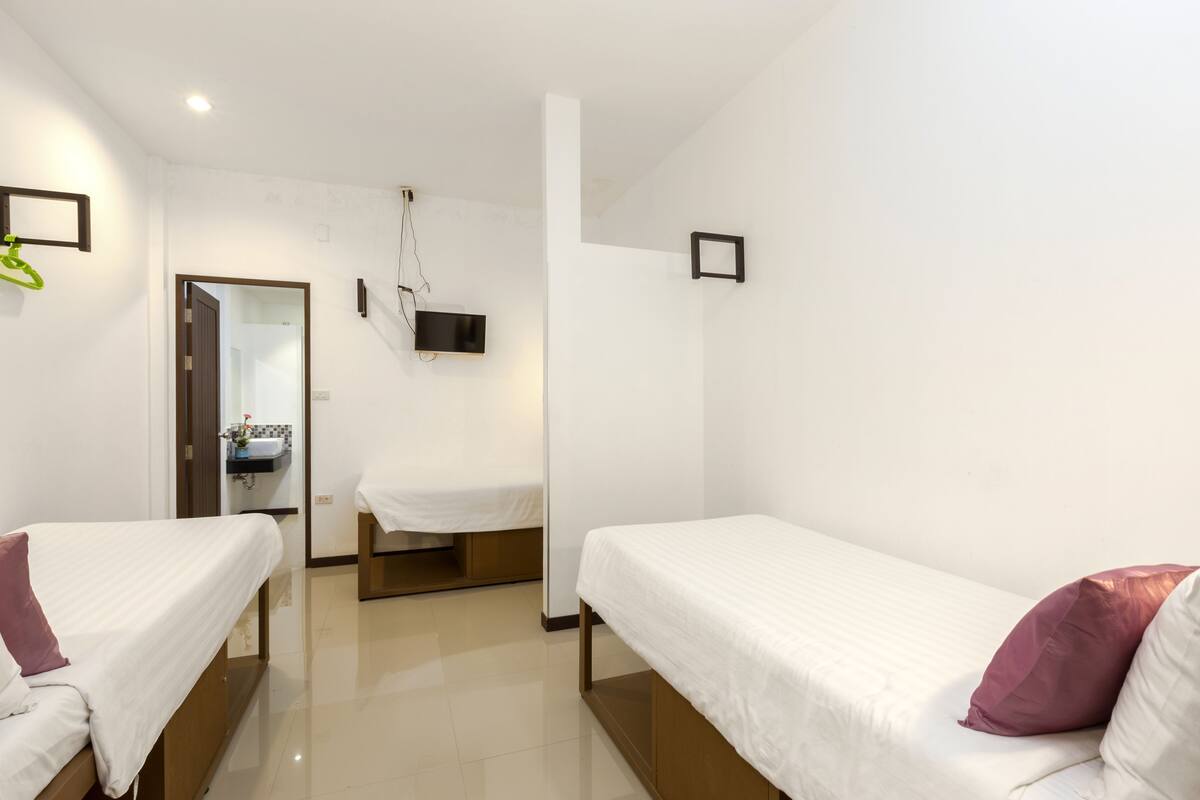A hotel room with two single beds, a small bathroom with a sink and mirror, and a door leading to another room.