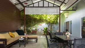 Ein überdachter Außenbereich mit einer Sitzecke, inklusive Sofa, Stühlen und Tisch, umgeben von viel Grün und einem Schild mit der Aufschrift "Lantern Hostel".