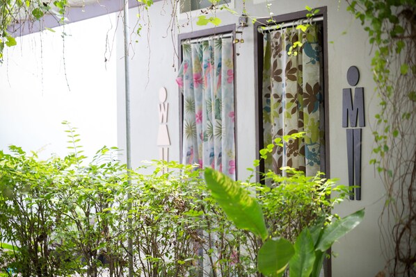 A building with a white exterior, a window with a floral curtain, and a wall with a symbol. - The Lantern Hostel and SPA (Chalong)