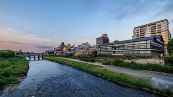 A riverside view of a cityscape with modern buildings, a bridge, and a pathway alongside the river.