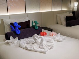 A hotel room with a neatly made bed, pillows, and decorative items including a blue and green balloon sculpture and a red and pink balloon flower.