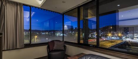 Una habitación moderna con un amplio ventanal que da a un paisaje urbano al atardecer.