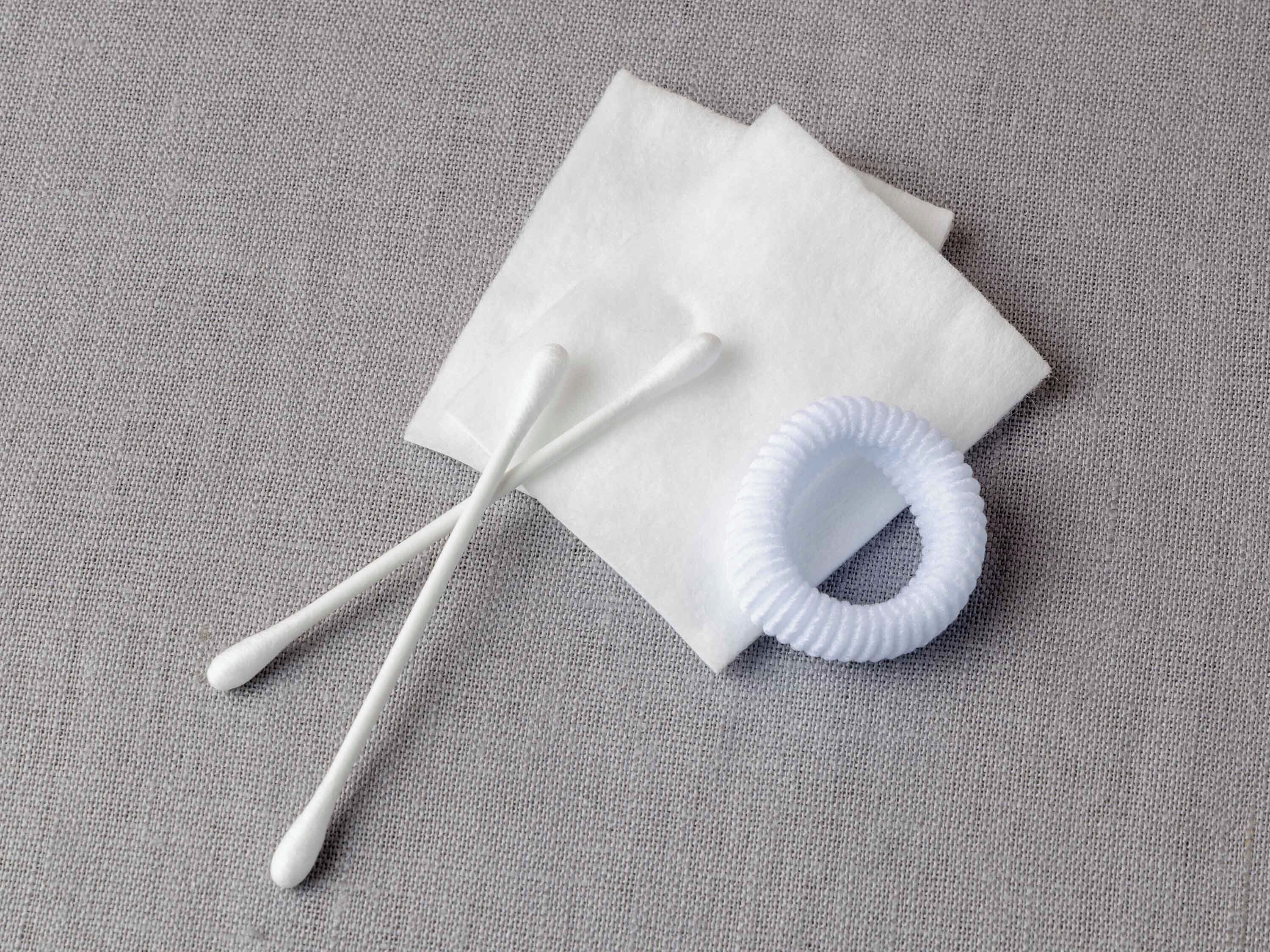 Ein Paar Wattestäbchen und ein weißes Papierhandtuch auf einer strukturierten grauen Oberfläche.