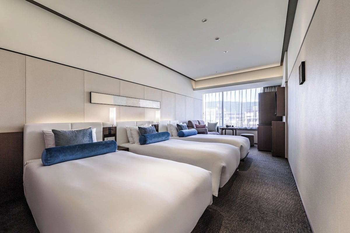 A hotel room with two beds, a desk, a chair, and a large window.