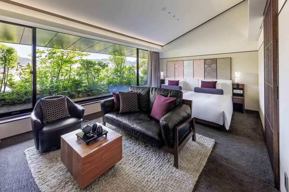 A modern hotel room with a large window, a bed, a sofa, and a coffee table.