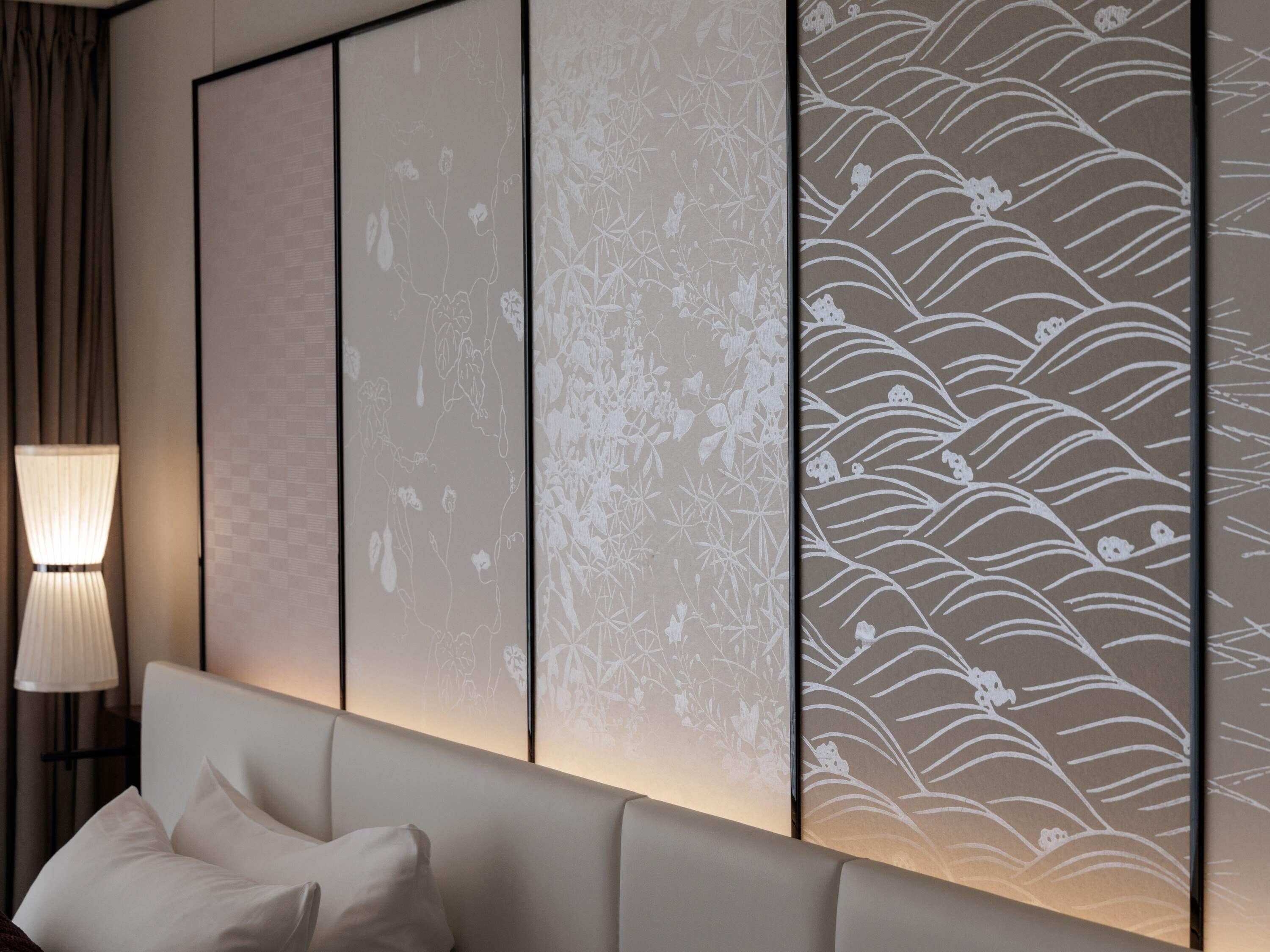 A room with a bed, a lamp, and a wall with a decorative screen.