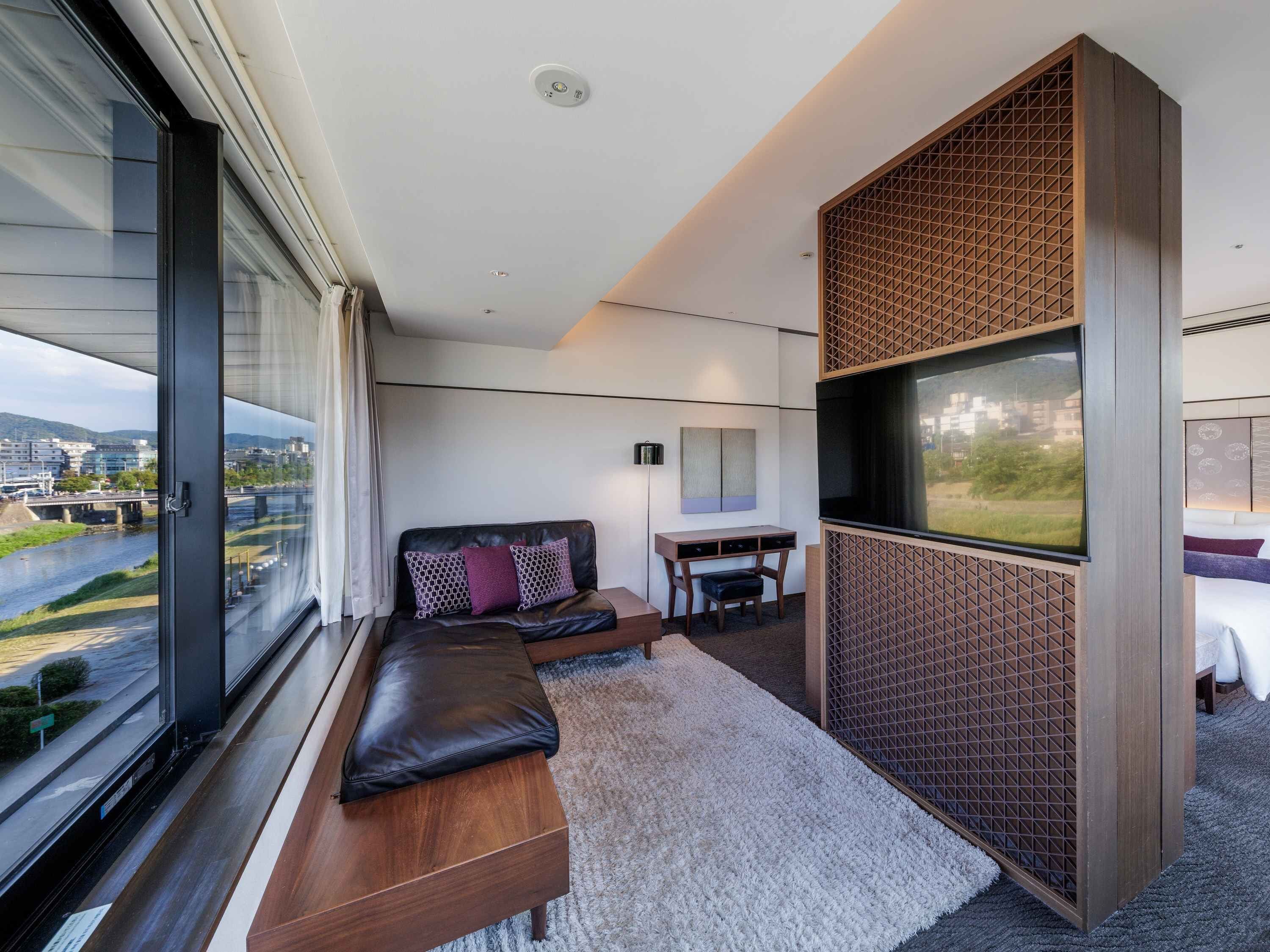 Una habitación de hotel moderna con un ventanal grande, un sofá, un escritorio y un televisor.