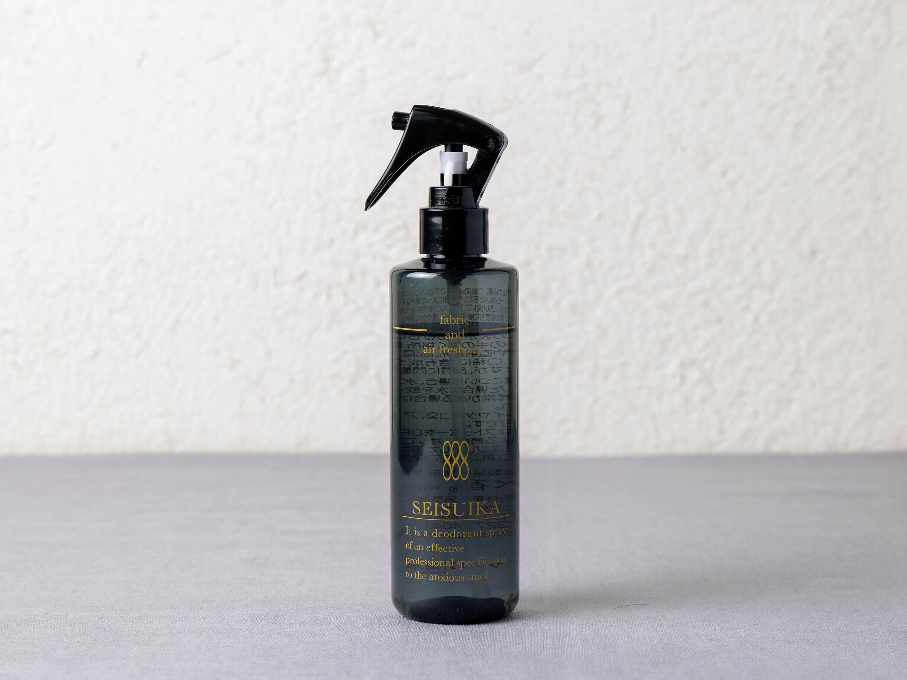 A black spray bottle with gold and white text on a textured grey surface.