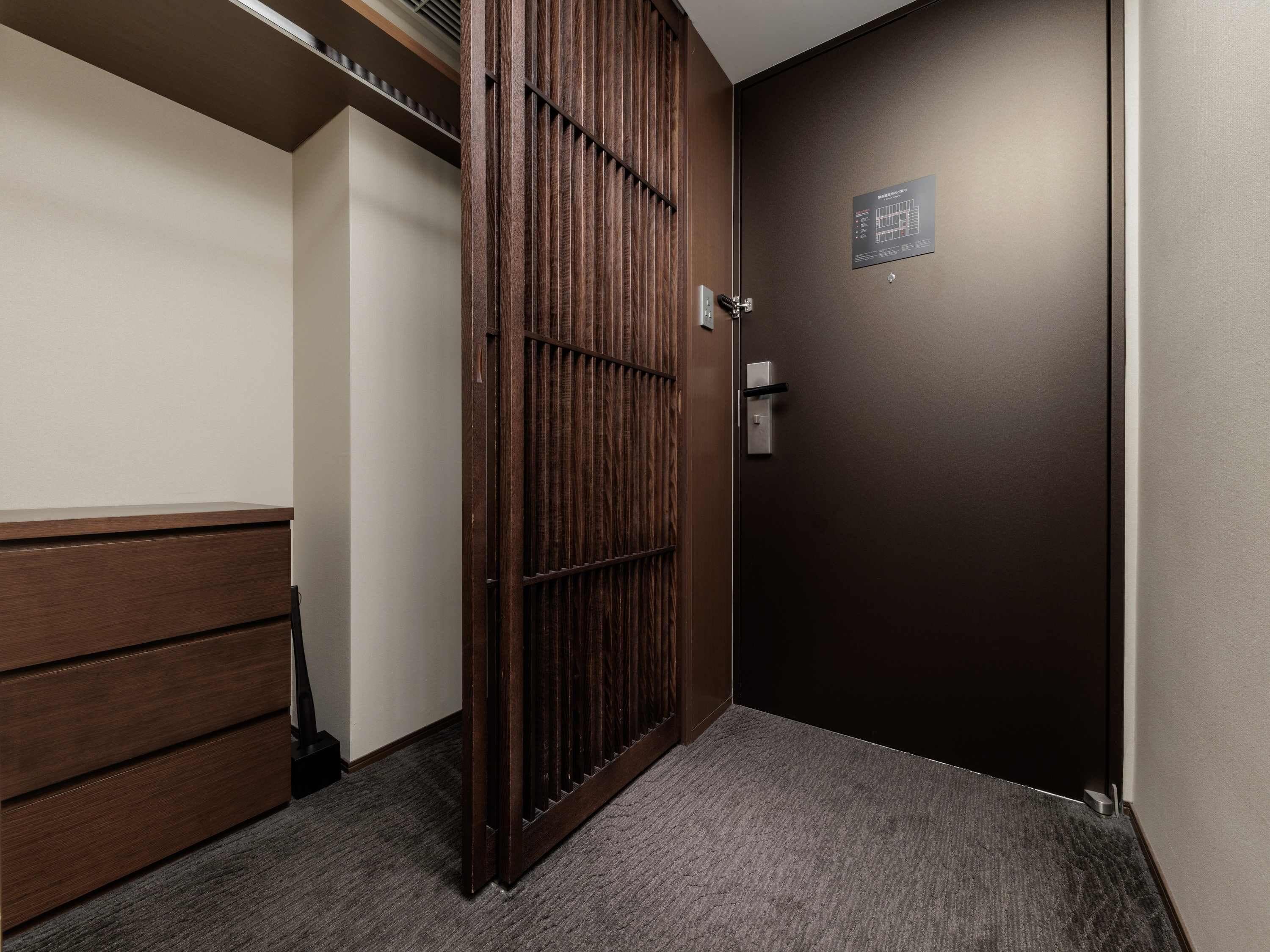 A room with a dark brown door, a wooden wardrobe, and a carpeted floor.