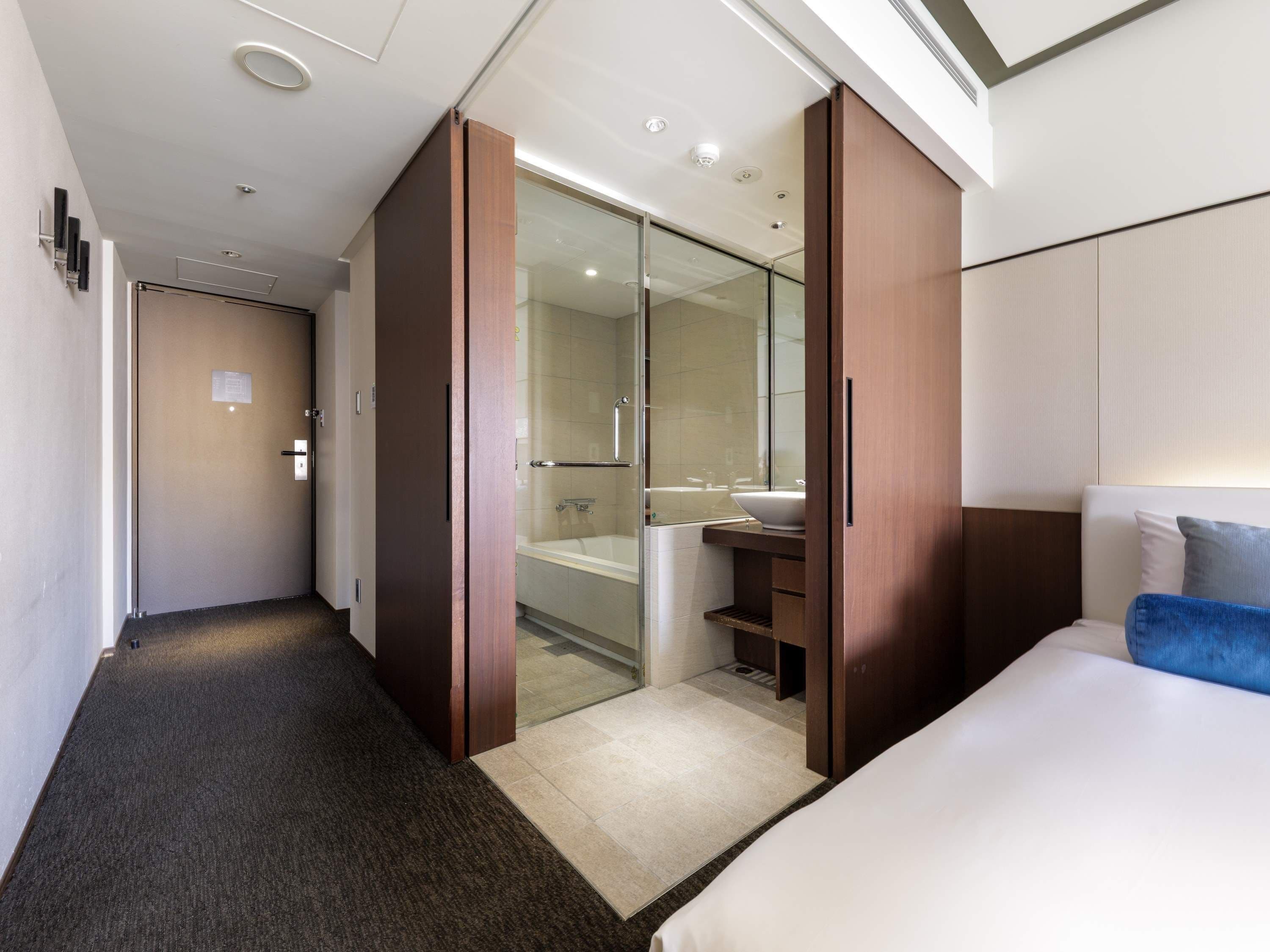 A hotel room with a large bed, a bathroom with a glass shower enclosure, and a wardrobe with sliding doors.