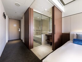 A hotel room with a large bed, a bathroom with a glass shower enclosure, and a wardrobe with sliding doors.
