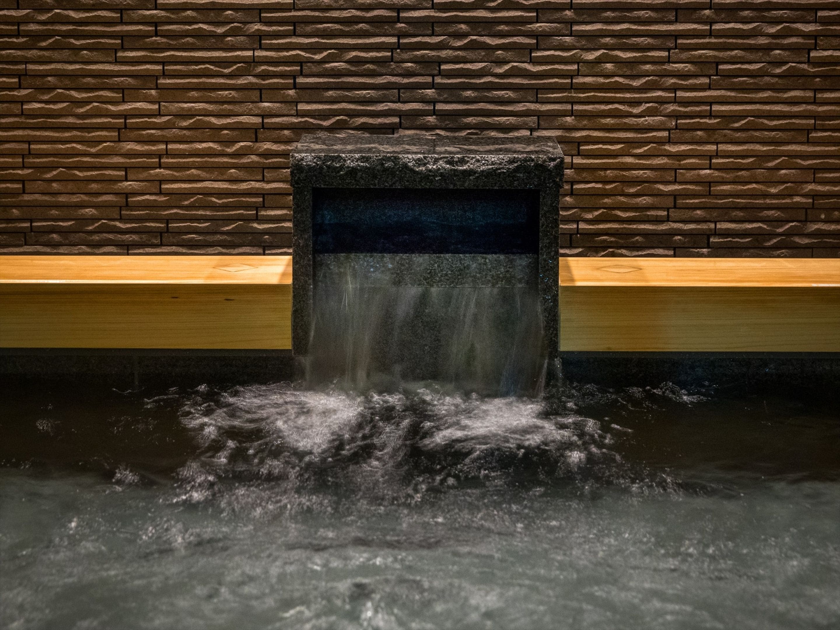 A stone water feature with a wooden bench and a stone wall in the background.