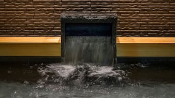 A stone water feature with a wooden bench and a stone wall in the background.