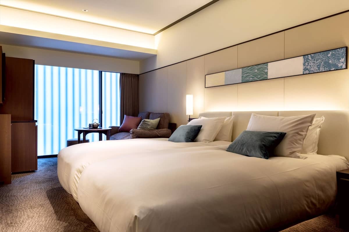 A hotel room with a large bed, a desk, a chair, and a window with blinds.