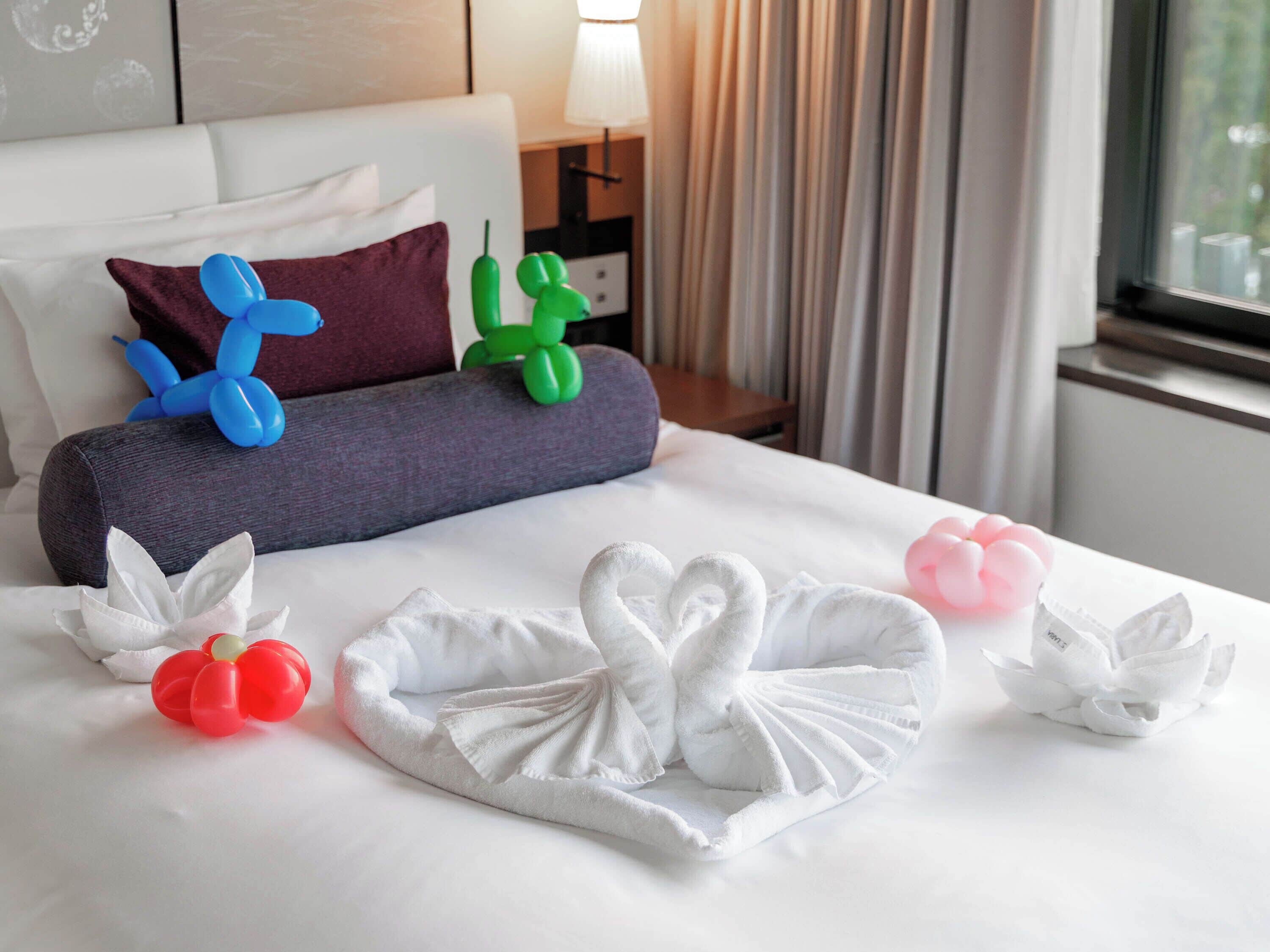 A hotel room with a neatly made bed, pillows, and decorative balloons.