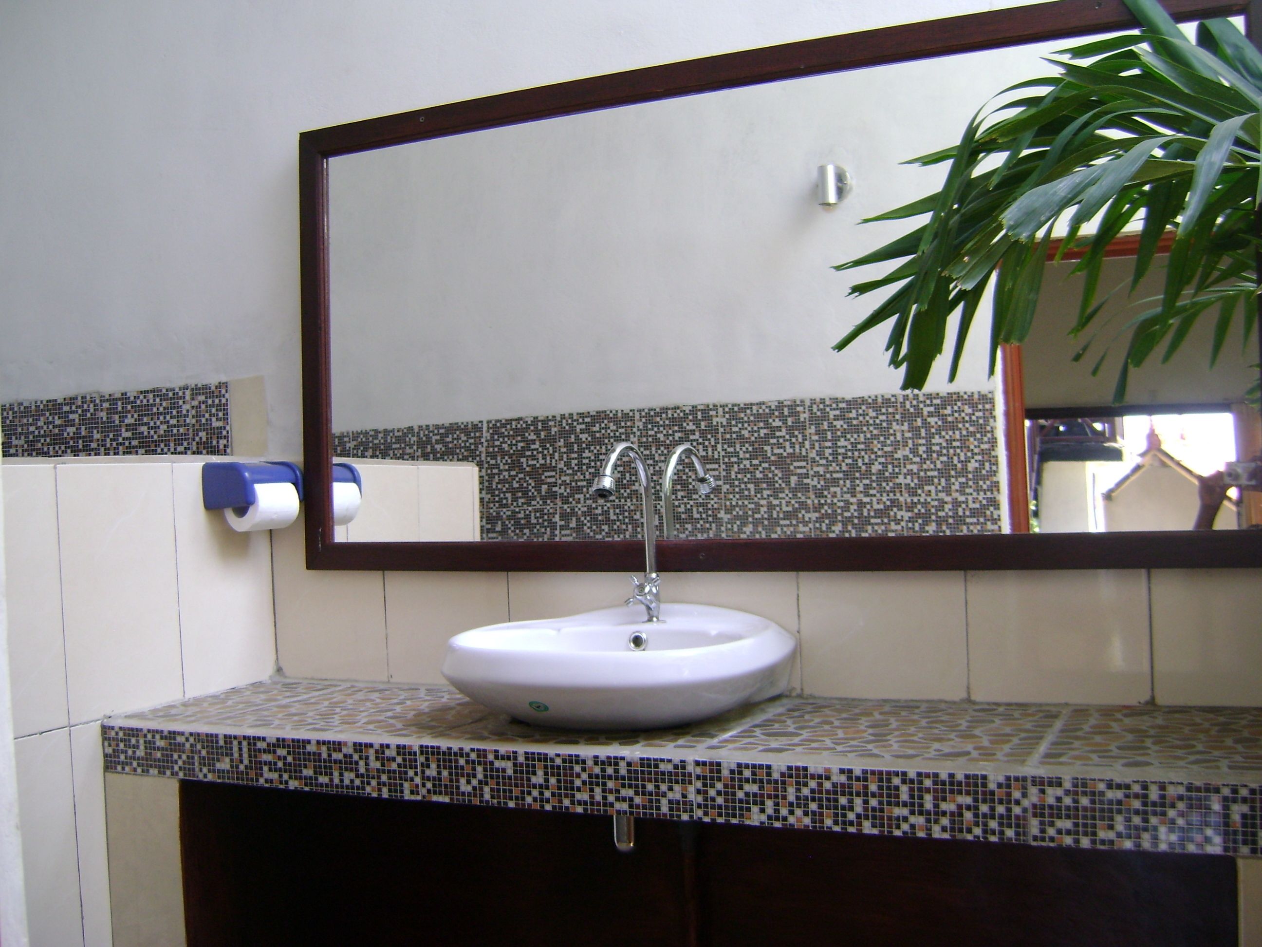 Un baño con un lavabo blanco, dos llaves, un espejo y un salpicadero de azulejos con diseño.