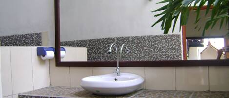 Un baño con un lavabo blanco, dos llaves, un espejo y un salpicadero de azulejos con diseño.