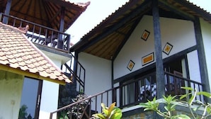 Um edifício de dois andares com varanda, telhado de telhas e escada de madeira.