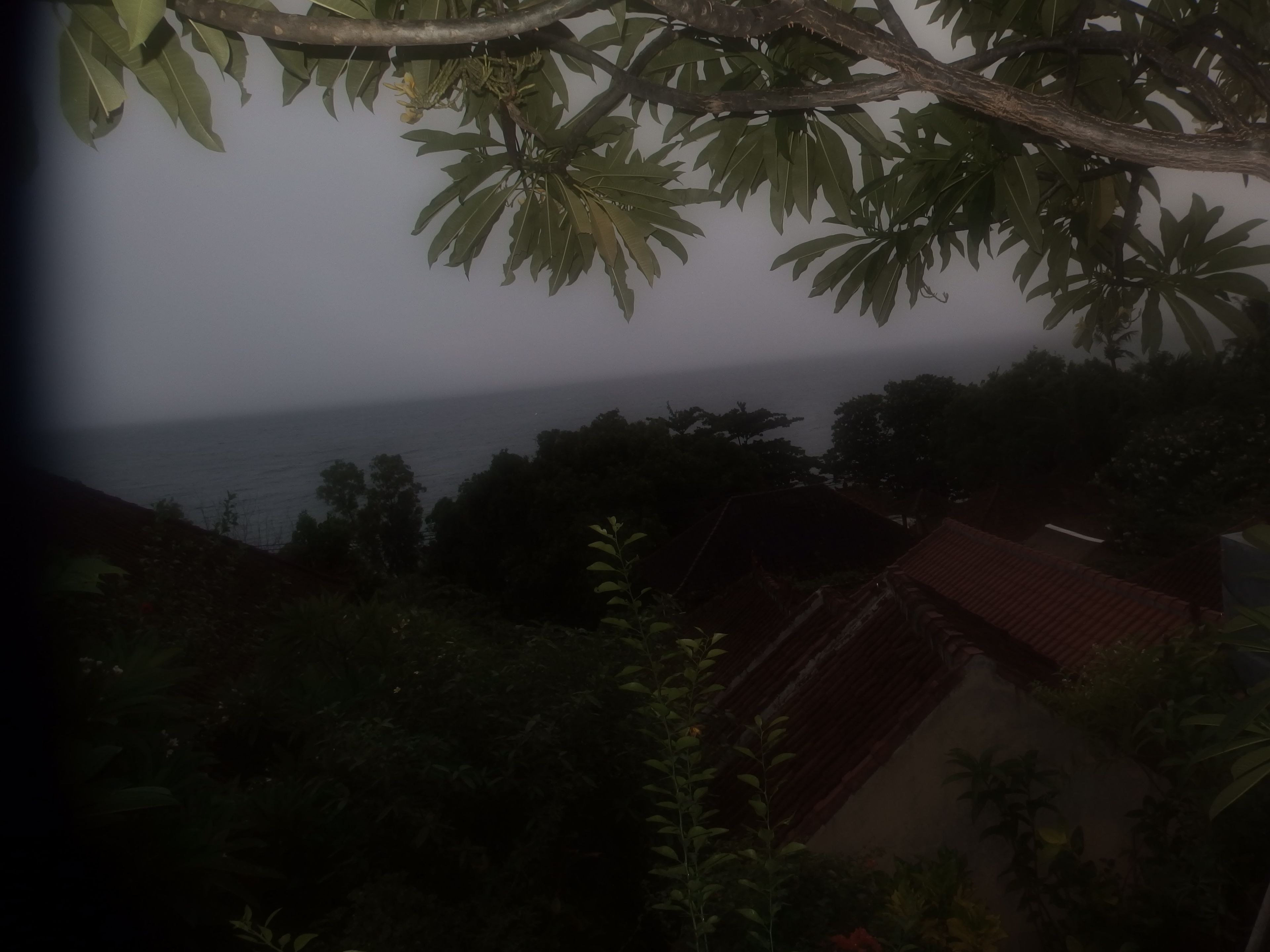 A view of a coastal area with a building that has a red roof, surrounded by greenery and trees.
