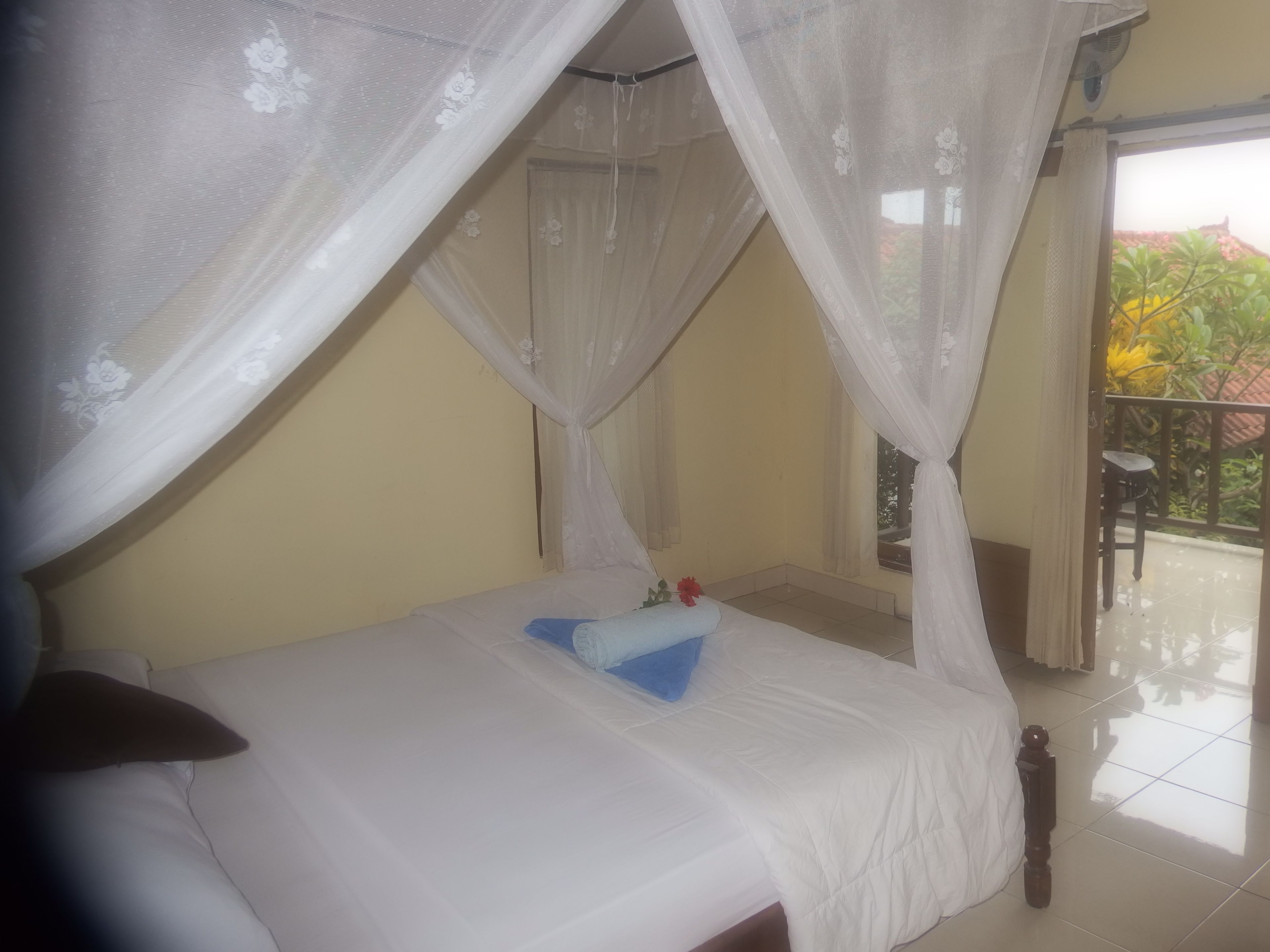 A bed with a canopy, a small table, and a view of the outside balcony.
