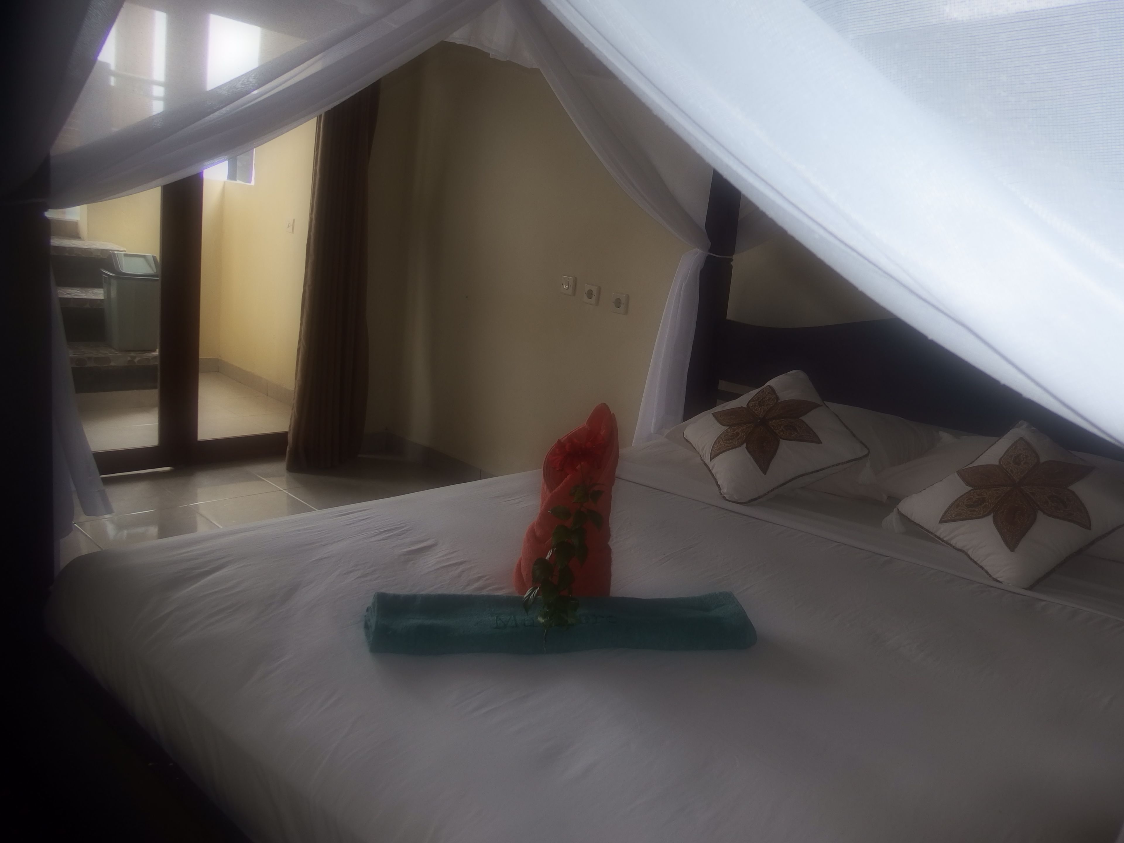A hotel room with a bed under a canopy, a red flower, and a blue towel.