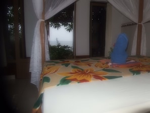 A room with a bed, a window with a view, and a curtain. - Bukit Indah Home Stay (Karangasem)