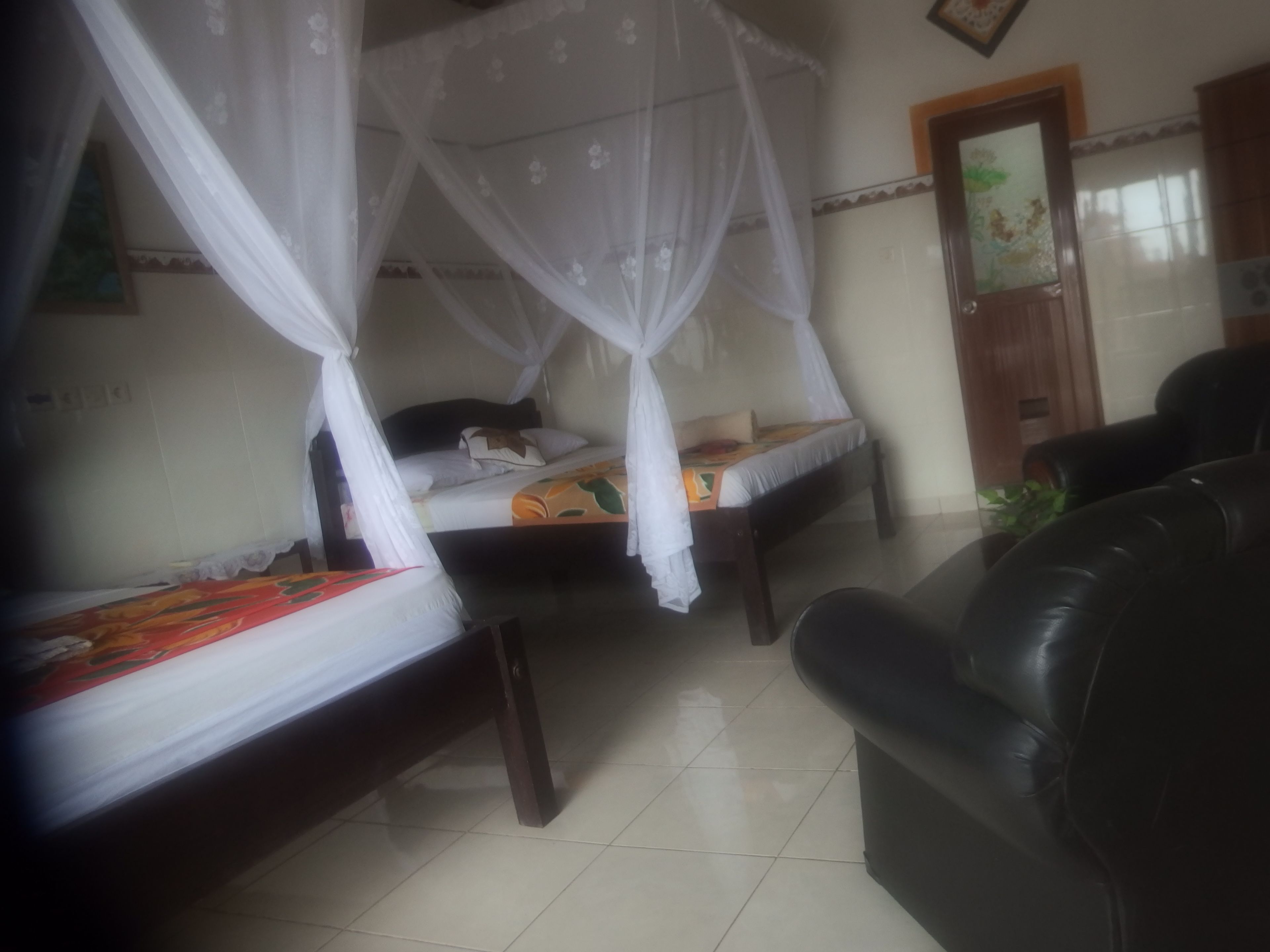 A room with two beds, each covered with a canopy, a black leather sofa, and a tiled floor.