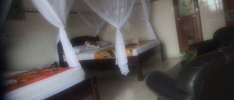 A room with two beds, each covered with a canopy, a black leather sofa, and a tiled floor.