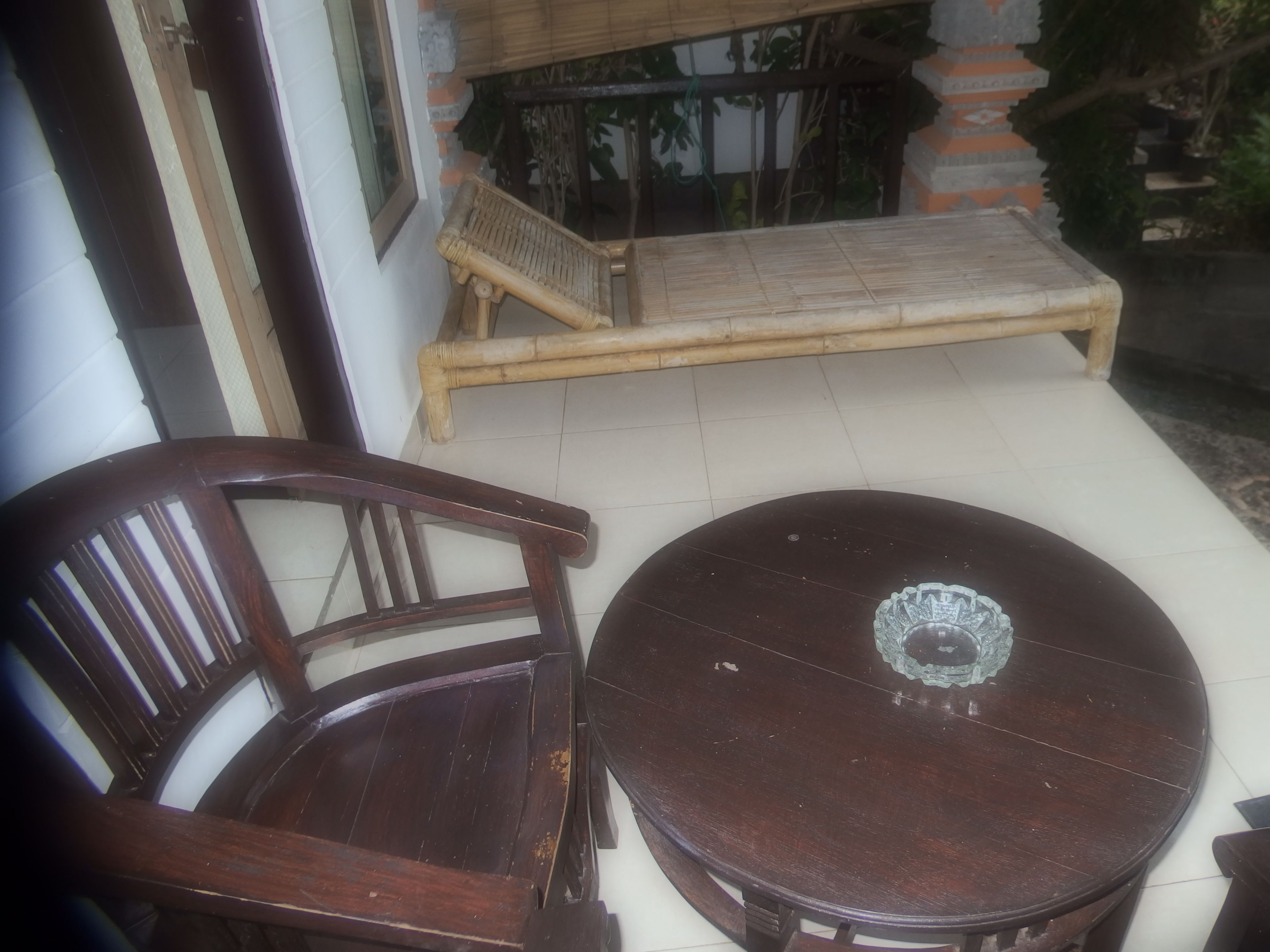 A wooden chair and table set on a tiled floor, with a wooden bench and potted plants in the background.