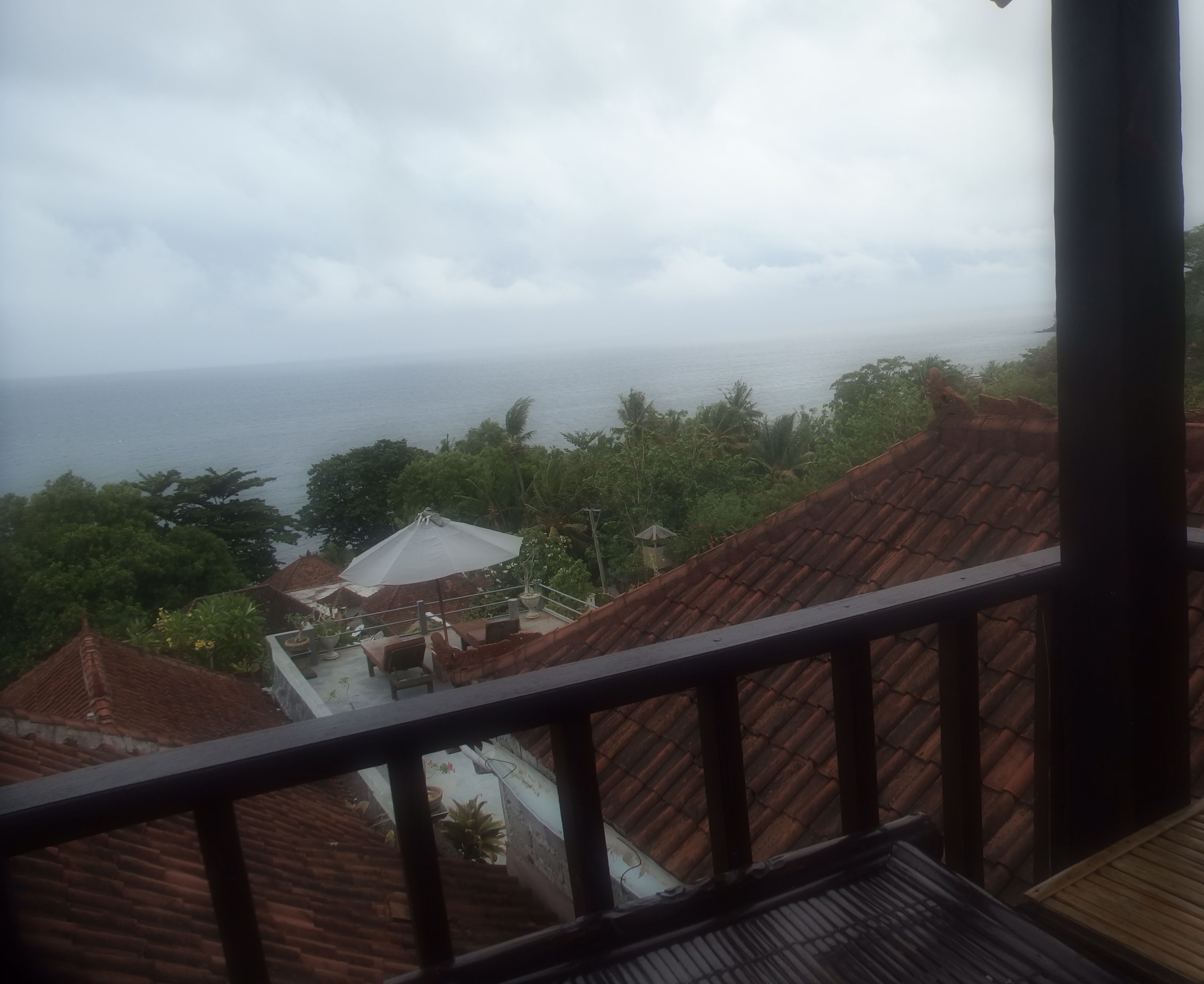 Blick vom Balkon auf eine Küstenlandschaft mit Meerblick, umgeben von Grünflächen und Gebäuden mit roten Ziegeldächern.