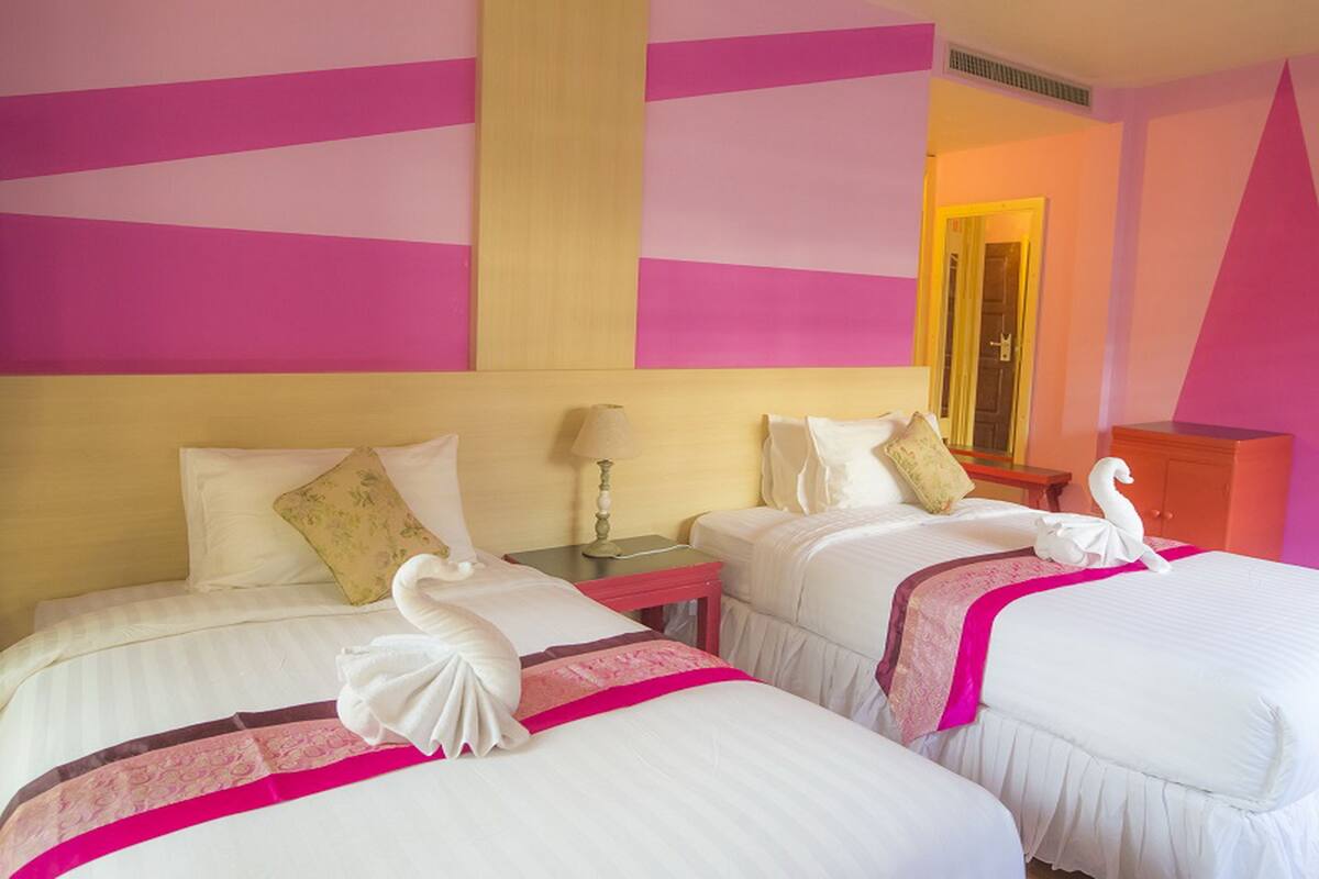 Une chambre d’hôtel avec deux lits, chacun agrémenté de draps blancs et de touches de rose, une tête de lit en bois, une table de chevet avec une lampe et un miroir.