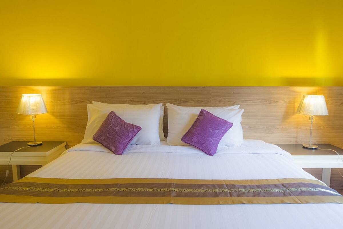 Une chambre d’hôtel avec un lit, deux tables de chevet, deux lampes et une tête de lit en bois.