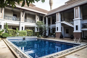 A swimming pool with a tiled edge, surrounded by a building with multiple balconies and a staircase.