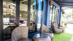 Wicker chairs and tables on artificial grass, large windows, and a view of the street. - Glur Chiangmai (Chiang Mai)