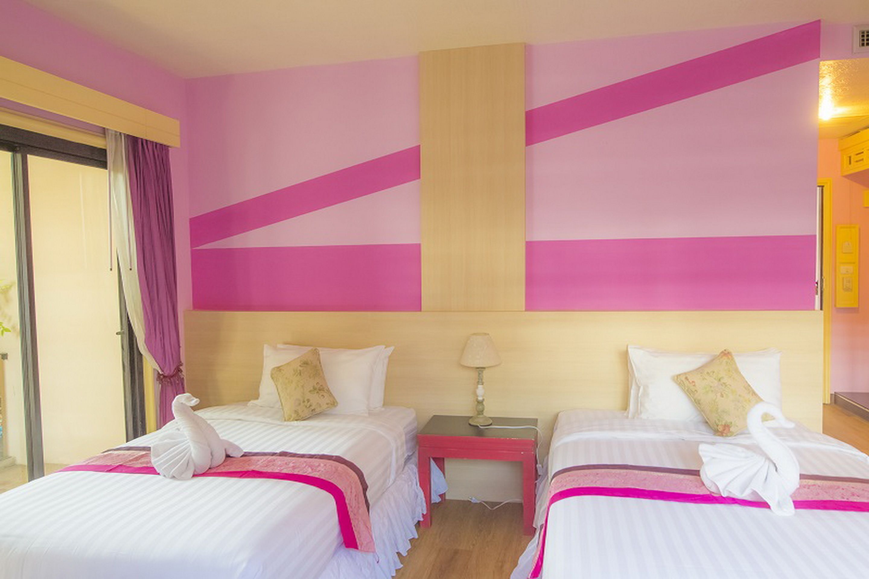 A hotel room with two beds, each with a swan-shaped towel, pink and yellow walls, and a wooden headboard.
