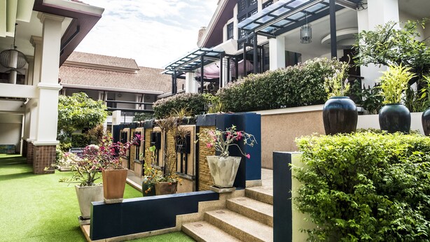 A courtyard with a green lawn, potted plants, and a staircase leading to a building with a glass roof. - Glur Chiangmai (Chiang Mai)