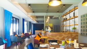 A modern restaurant with wooden tables and chairs, a brick accent wall, and a bar area. - Glur Chiangmai (Chiang Mai)