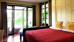 Un dormitorio con una cama grande, un banco y vistas a zonas verdes por la ventana.